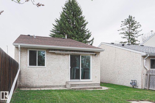 Rear exterior featuring textured stucco siding, a brown shingle roof, a sliding glass patio door, and a single-pane window - 35 Chungo Drive, Devon, AB - Outdoor