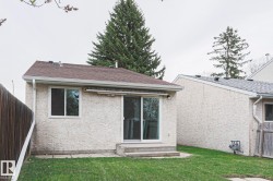 Rear exterior featuring textured stucco siding, a brown shingle roof, a sliding glass patio door, and a single-pane window - 
