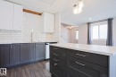Kitchen featuring two-tone cabinetry with white upper cabinets and dark lower cabinets, white subway tile backsplash, light countertops, a kitchen island with storage, and wood-finish flooring - 35 Chungo Drive, Devon, AB  - Indoor Photo Showing Kitchen With Upgraded Kitchen 