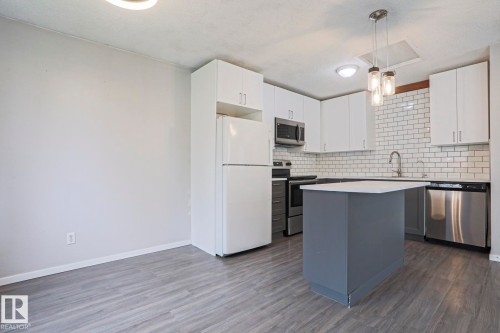 Kitchen featuring a central island with countertop, white cabinetry, stainless steel appliances, subway tile backsplash, and wood-finish flooring - 35 Chungo Drive, Devon, AB - Indoor Photo Showing Kitchen With Upgraded Kitchen
