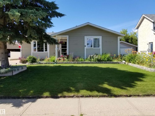 The property features a well-maintained lawn, framed by garden beds with various plantings and flowers - 13332 25 Street, Edmonton, AB - Outdoor