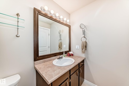 Bathroom featuring a vanity with a white basin and a light-toned countertop, a framed mirror with overhead lighting, and glass shelving - 13332 25 Street, Edmonton, AB - Indoor Photo Showing Bathroom