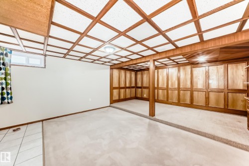 Spacious room featuring a tiered floor plan with carpet and tile, wood paneling, and a grid ceiling design - 13332 25 Street, Edmonton, AB - Indoor Photo Showing Other Room