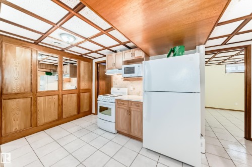Kitchenette area featuring white tile flooring, wood paneling, and a white refrigerator - 13332 25 Street, Edmonton, AB - Indoor Photo Showing Kitchen