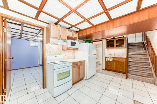 Kitchen area featuring white tile flooring, light wood cabinetry, white appliances, and a drop-in ceiling - 13332 25 Street, Edmonton, AB - Indoor Photo Showing Kitchen