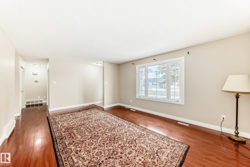 Living area with polished hardwood floors, light-toned walls, and a large window providing views of the outdoors - 13332 25 Street, Edmonton, AB - Indoor Photo Showing Other Room