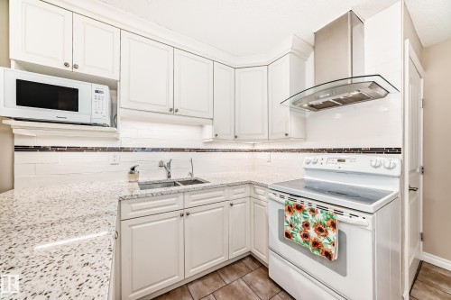 The kitchen features white cabinetry, granite countertops, a double basin sink, and a range with an overhead vent hood - 13332 25 Street, Edmonton, AB - Indoor Photo Showing Kitchen With Double Sink