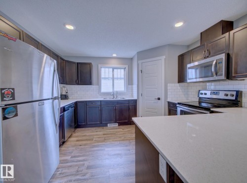 Kitchen featuring dark wood-finish cabinetry, white subway tile backsplash, stainless steel appliances, light-toned countertops, and wood-finish flooring - 11 165 Cy Becker Boulevard, Edmonton, AB - Indoor Photo Showing Kitchen With Stainless Steel Kitchen With Double Sink
