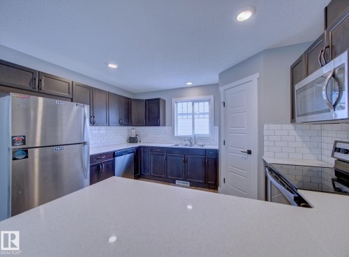 Kitchen featuring dark cabinetry, stainless steel appliances, white subway tile backsplash, light-toned countertops, and recessed lighting - 11 165 Cy Becker Boulevard, Edmonton, AB - Indoor Photo Showing Kitchen With Stainless Steel Kitchen With Upgraded Kitchen