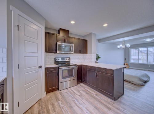 L-shaped kitchen with dark wood cabinetry, white countertops, and subway tile backsplash - 11 165 Cy Becker Boulevard, Edmonton, AB - Indoor Photo Showing Kitchen