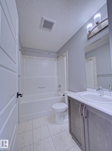 Upper 4PC Bathroom featuring a white bathtub with a tiled surround, a toilet, and a vanity with a white countertop and oval sink - 11 165 Cy Becker Boulevard, Edmonton, AB - Indoor Photo Showing Bathroom