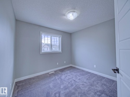 Room featuring textured carpet flooring, light gray wall paint, and white baseboards - 11 165 Cy Becker Boulevard, Edmonton, AB - Indoor Photo Showing Other Room