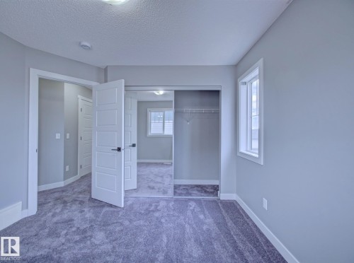 Neutral-toned room featuring a window with white trim, gray plush carpet, and light gray walls - 11 165 Cy Becker Boulevard, Edmonton, AB - Indoor Photo Showing Other Room