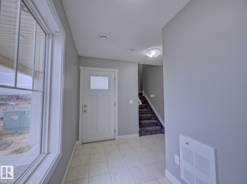 Entryway featuring a white paneled door with frosted glass, ceramic tile flooring, and a window with exterior views - 11 165 Cy Becker Boulevard, Edmonton, AB - Indoor Photo Showing Other Room