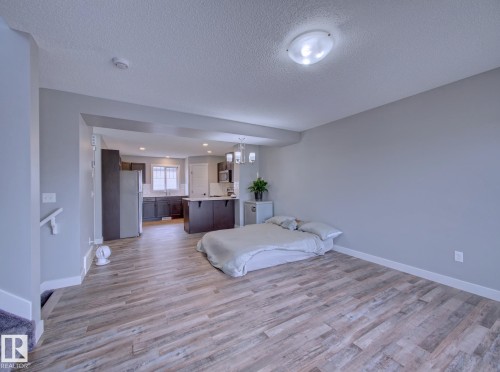 Open-concept living area featuring wood-finish flooring, recessed lighting, and a modern kitchen with dark cabinetry and stainless steel appliances - 11 165 Cy Becker Boulevard, Edmonton, AB - Indoor Photo Showing Bedroom