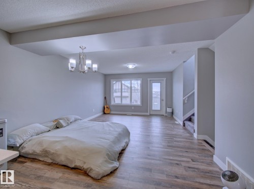 Spacious open-concept room featuring wood-finish flooring, light gray wall paint, and a modern chandelier - 11 165 Cy Becker Boulevard, Edmonton, AB - Indoor Photo Showing Bedroom