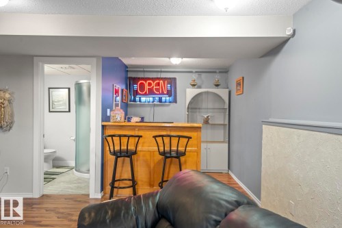 Wood-finish flooring in a finished lower level featuring a built-in wet bar with two bar stools and an arched display cabinet - 1304 12 Street, Cold Lake, AB - Indoor Photo Showing Other Room