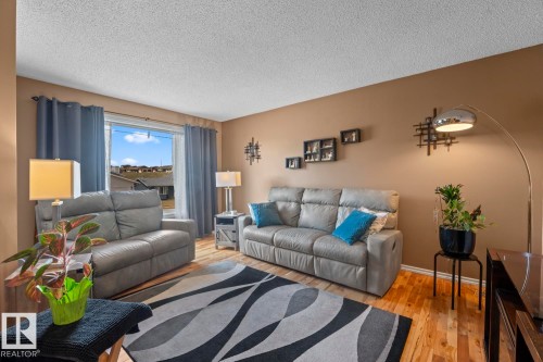 Spacious living area featuring light wood-finish flooring, a neutral wall color, and a large window with blue curtains - 1304 12 Street, Cold Lake, AB - Indoor Photo Showing Living Room
