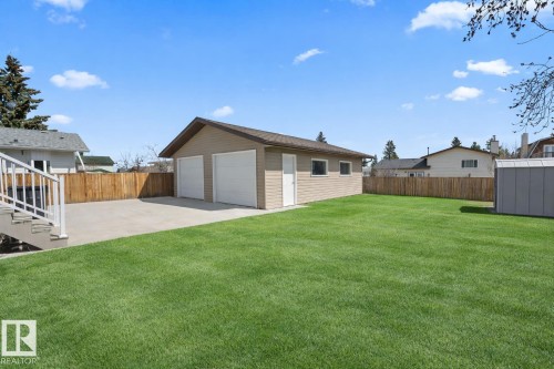 Expansive green lawn with a detached two-car garage featuring two white garage doors and a separate entry door - 1304 12 Street, Cold Lake, AB - Outdoor