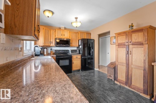 Kitchen featuring natural wood cabinetry, mottled countertops, black appliances, and textured backsplash - 1304 12 Street, Cold Lake, AB - Indoor Photo Showing Kitchen