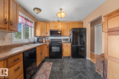 Kitchen featuring wood cabinetry, black appliances, a double basin sink, and laminate countertops - 1304 12 Street, Cold Lake, AB - Indoor Photo Showing Kitchen With Double Sink