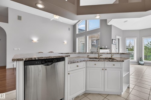 Open-concept kitchen featuring an island with granite countertops, integrated stainless steel dishwasher, and a double basin sink with a gooseneck faucet - 201 Erin Ridge Drive, St. Albert, AB - Indoor