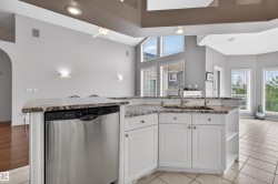 Open-concept kitchen featuring an island with granite countertops, integrated stainless steel dishwasher, and a double basin sink with a gooseneck faucet - 