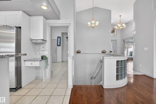 Open foyer featuring hardwood flooring, a curved staircase with glass block accents, and two chandelier light fixtures - 201 Erin Ridge Drive, St. Albert, AB - Indoor Photo Showing Kitchen