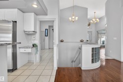 Open foyer featuring hardwood flooring, a curved staircase with glass block accents, and two chandelier light fixtures - 