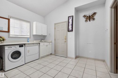 Dedicated utility space featuring tile flooring, a built-in sink, white cabinetry, a window with blinds, and a solid entry door - 201 Erin Ridge Drive, St. Albert, AB - Indoor Photo Showing Laundry Room