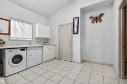 Dedicated utility space featuring tile flooring, a built-in sink, white cabinetry, a window with blinds, and a solid entry door - 