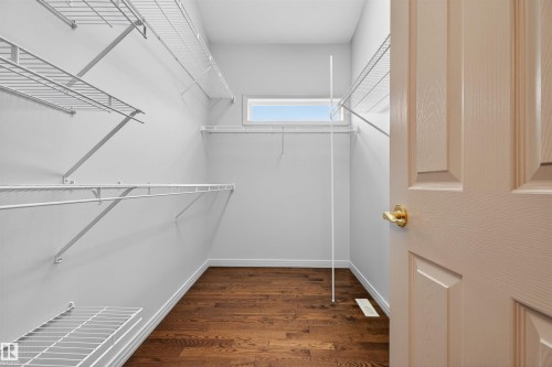 Walk-in closet featuring wood-finish flooring, white wire shelving, a high transom window, and a paneled door with brass hardware - 201 Erin Ridge Drive, St. Albert, AB - Indoor With Storage