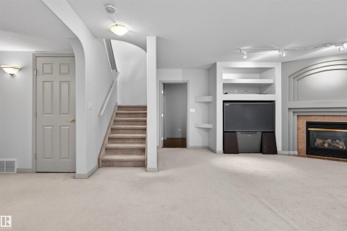 Spacious room featuring light-toned carpeting, a built-in entertainment center with shelving, a fireplace with a tile surround, and a carpeted staircase - 201 Erin Ridge Drive, St. Albert, AB - Indoor With Fireplace