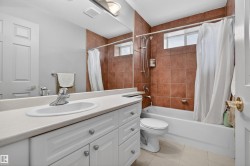 Bathroom featuring a white vanity with integrated sink, a large mirror, a shower-over-tub combination with brown tile surround, and a frosted window - 
