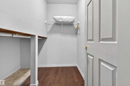 Walk-in closet featuring wire shelving, wood-finish flooring, and a white paneled door with a brass-finish doorknob - 201 Erin Ridge Drive, St. Albert, AB - Indoor