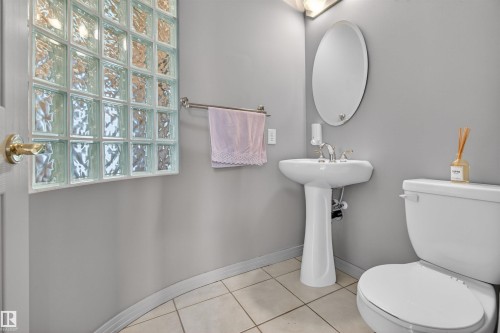 Bathroom featuring a glass block window, pedestal sink, oval wall mirror, and tile flooring - 201 Erin Ridge Drive, St. Albert, AB - Indoor Photo Showing Bathroom