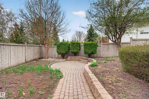 Brick paver patio with a curved retaining wall and circular design, complemented by a paver pathway and perimeter fencing - 201 Erin Ridge Drive, St. Albert, AB - Outdoor