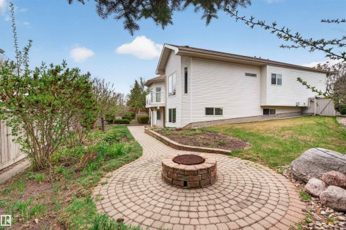 Expansive backyard featuring a circular paver patio with a built-in fire pit, a curved paver pathway, and a variety of mature plantings - 201 Erin Ridge Drive, St. Albert, AB - Outdoor