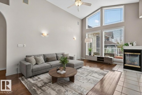 Vaulted ceiling living room featuring a fireplace with a white mantel, large windows with blinds, wood-finish flooring, and a ceiling fan - 201 Erin Ridge Drive, St. Albert, AB - Indoor Photo Showing Living Room With Fireplace