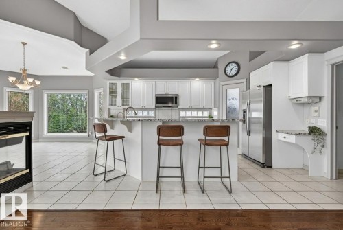 Modern kitchen featuring white cabinetry, stainless steel appliances, a granite-finish island with seating, and a tile backsplash - 201 Erin Ridge Drive, St. Albert, AB - Indoor Photo Showing Kitchen