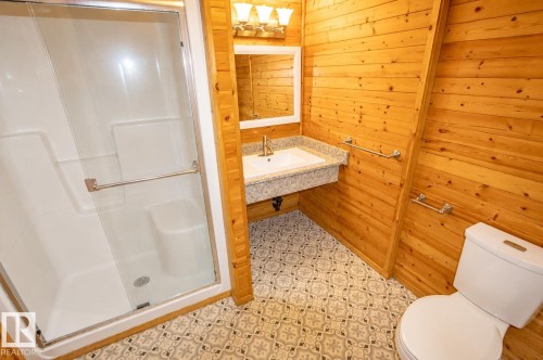 Bathroom featuring a glass-enclosed shower, wood-paneled walls, a vanity with a stone countertop, and patterned floor tiles - 4510 Lakeshore Dr, St. Paul Town, AB - Indoor Photo Showing Bathroom