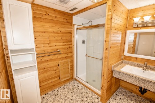Bathroom featuring patterned tile flooring, wood-finish wall paneling, a glass-enclosed shower, a vanity with a stone-finish countertop and integrated sink, and white built-in cabinetry with open shelving - 4510 Lakeshore Dr, St. Paul Town, AB - Indoor Photo Showing Bathroom