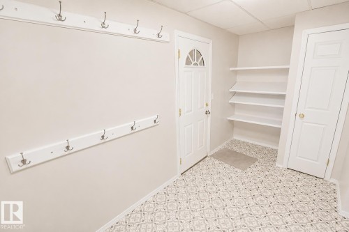 Entry area featuring patterned floor tile, white built-in shelving, two white coat racks with multiple hooks, a paneled door with a half-moon window, and a white interior door with a brass knob - 4510 Lakeshore Dr, St. Paul Town, AB - Indoor Photo Showing Other Room