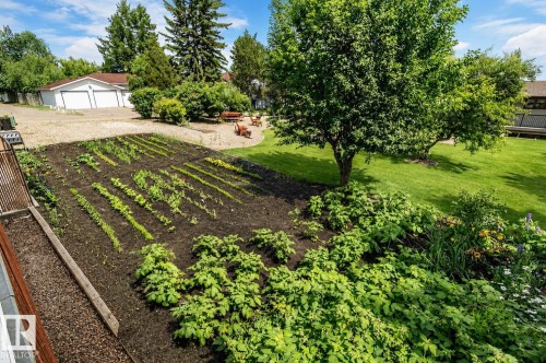 Spacious backyard featuring a cultivated garden plot with multiple rows of plants, mature trees, a manicured lawn, and a detached two-car garage with white doors - 4510 Lakeshore Dr, St. Paul Town, AB - Outdoor