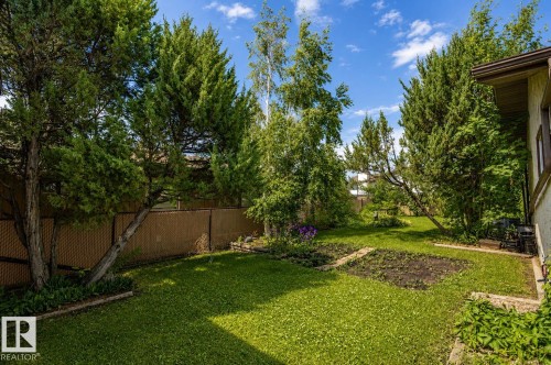 Landscaped backyard featuring established trees, a manicured lawn, a garden bed, and a privacy fence - 4510 Lakeshore Dr, St. Paul Town, AB - Outdoor