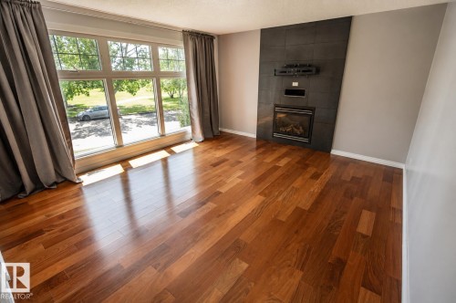 Expansive living space featuring wood-finish flooring, a large picture window, and a built-in fireplace with a tiled surround - 4510 Lakeshore Dr, St. Paul Town, AB - Indoor With Fireplace