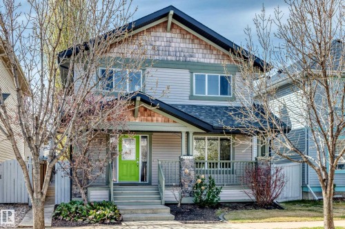 Two-story residence featuring siding and shingle accents, a covered front porch with stone pillars, and a vibrant green entry door - 5333 Terwillegar Boulevard, Edmonton, AB - Outdoor With Deck Patio Veranda