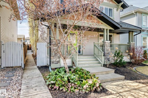 Front exterior featuring a covered porch with stone-clad columns, a wood-finish railing, and concrete steps - 5333 Terwillegar Boulevard, Edmonton, AB - Outdoor With Deck Patio Veranda