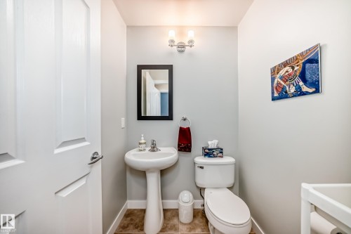 Powder room featuring a pedestal sink with a chrome faucet, a rectangular framed mirror, and a white toilet - 5333 Terwillegar Boulevard, Edmonton, AB - Indoor Photo Showing Bathroom