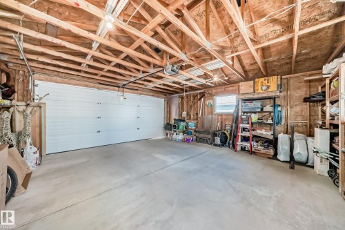 Spacious garage featuring a white sectional garage door, exposed wood rafters, concrete flooring, and a single window - 5333 Terwillegar Boulevard, Edmonton, AB - Indoor Photo Showing Garage